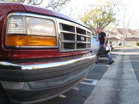 1995 Ford F-150 - A man walks past the front of a red 1995 Ford F-150 truck parked in a lot.