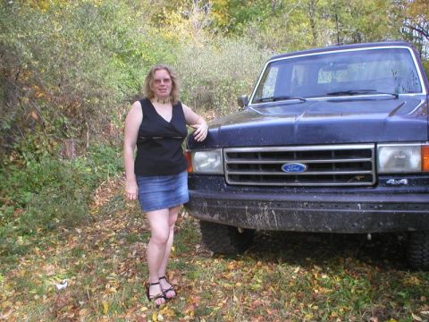 1989 Ford Bronco - A person stands beside the front fender of a dirty dark blue late-80s Ford Bronco parked on a leaf-covered woodland edge in autumn. The tru…
