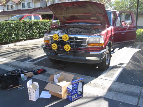 1995 Ford F-150 - A red 1995 Ford F-150 is parked with its hood open, displaying smiley face auxiliary lights and various tools nearby.
