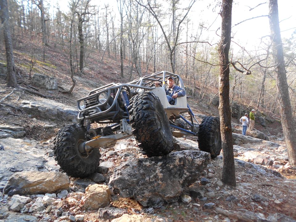Custom off-road buggy with large tires navigating a rocky incline in a wooded area