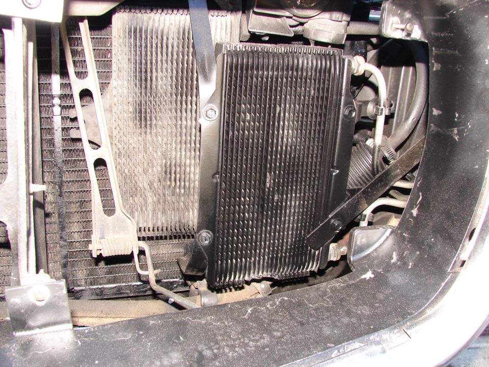 Transmission cooler mounted in front of radiator, with hoses and brackets visible