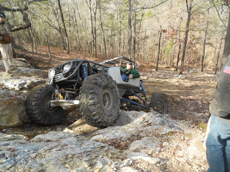 Off-road buggy with large tires navigating rocky terrain. Driver in green jacket visible