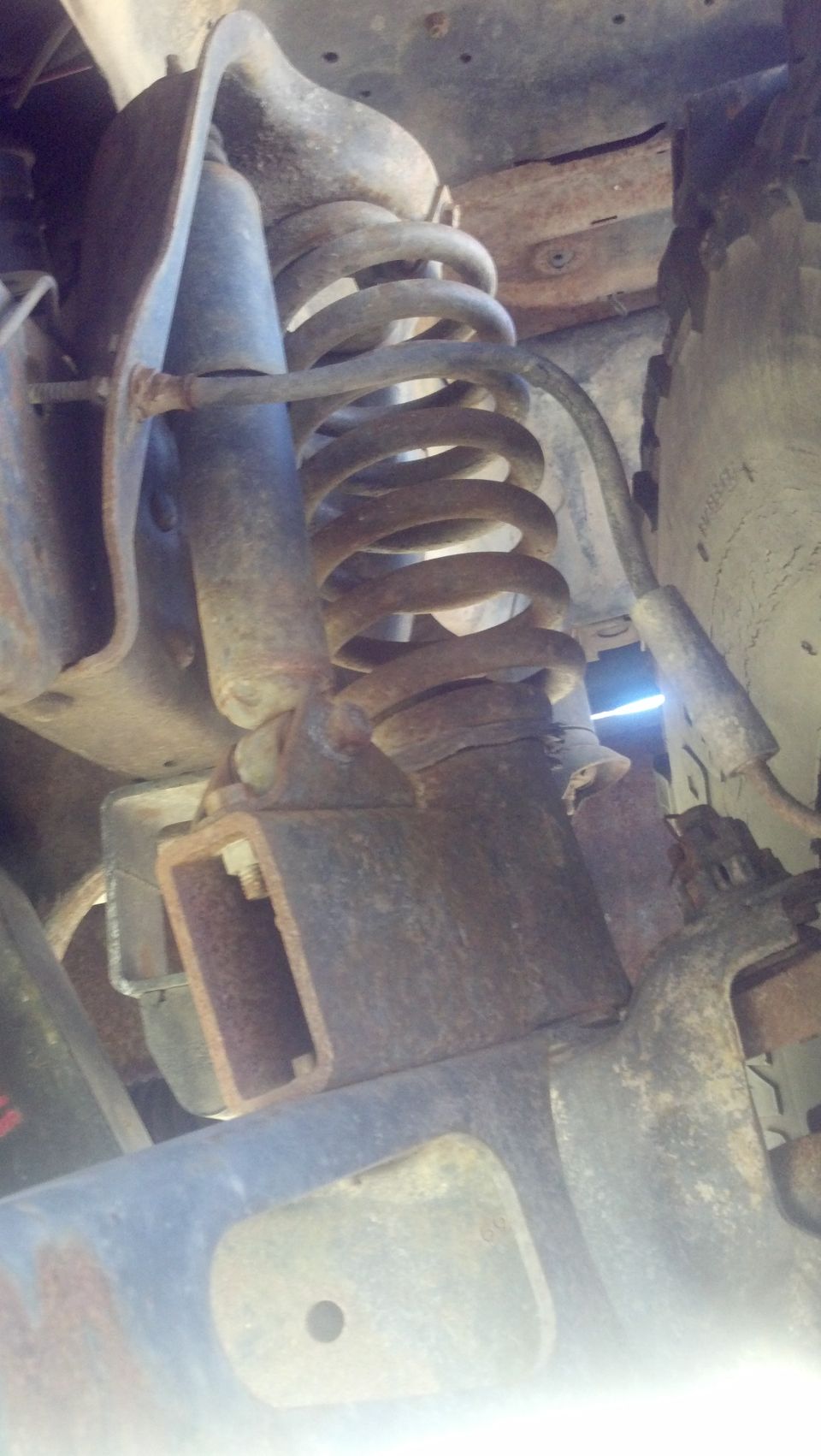 Close-up of rusty truck suspension parts, including a coil spring and shock absorber