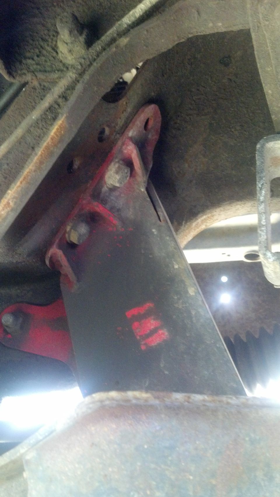 Red painted metal bracket with red stencil markings attached to a rusty undercarriage