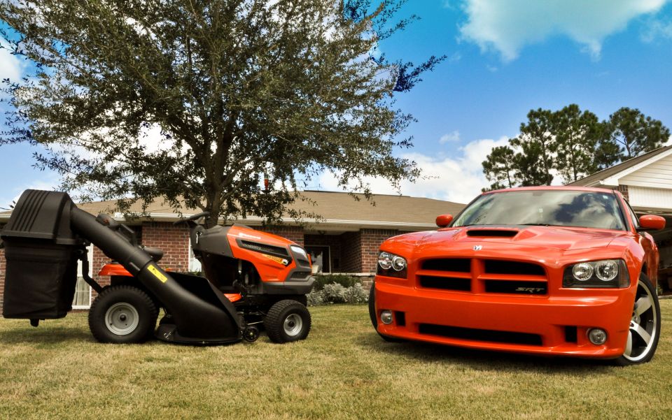 Orange 2009 Dodge Charger SRT parked on grass next to a riding mower