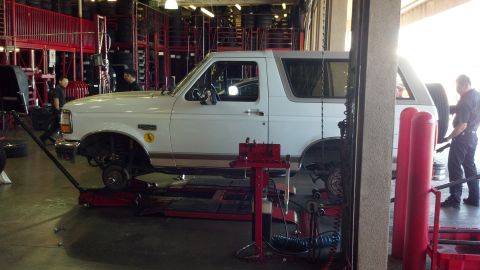 1996 Ford Bronco - A white 1996 Ford Bronco SUV is being serviced in a garage, with its front wheels off.