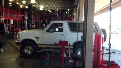1996 Ford Bronco - A white 1996 Ford Bronco is shown on a lift inside a garage, possibly undergoing maintenance.