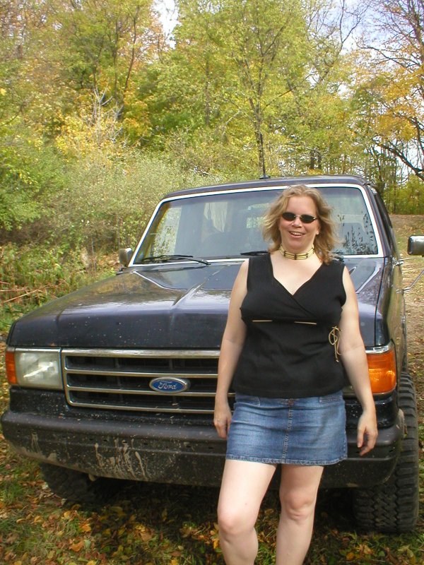 Person standing in front of muddy dark blue Ford truck grille on autumn trail