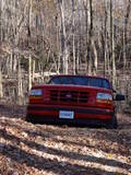 1995 Ford Bronco - A red pickup truck is parked on a dirt path surrounded by trees in the woods.