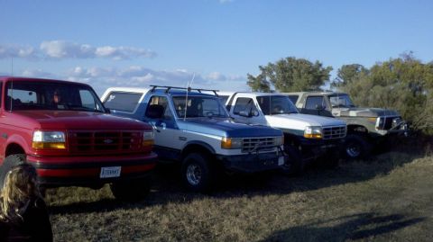 1995 Ford Bronco - Several Ford Broncos are lined up outdoors under a partly cloudy sky.
