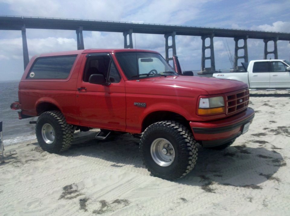 Red 1995 Ford Bronco on beach with bridge in background