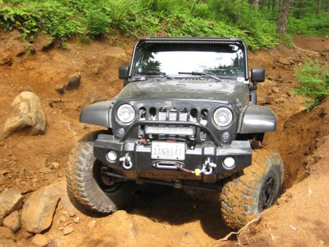 2008 Jeep Wrangler - Jeep Wrangler tackling a challenging off-road obstacle with mud-covered tires.