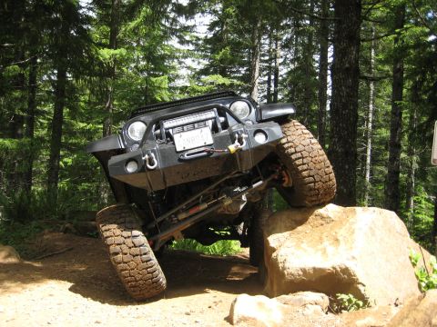 2008 Jeep Wrangler - A modified Jeep Wrangler navigates a challenging rocky obstacle on a wooded trail.