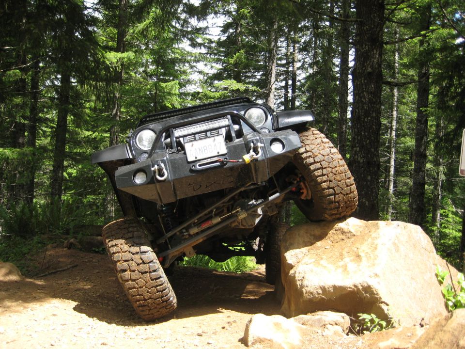 Jeep Wrangler climbing over a rock on a trail, front end angled up