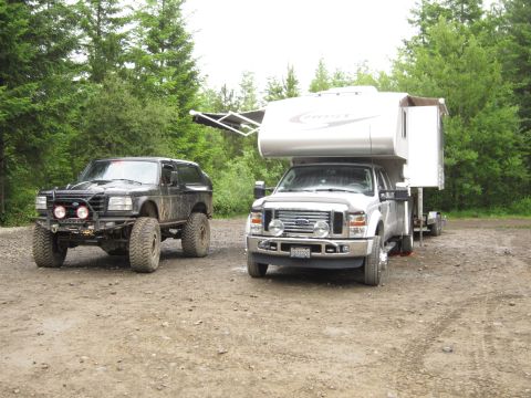 1996 Ford Bronco - Two trucks, a modified Bronco and a Ford F-series with a camper, are parked on a dirt road.