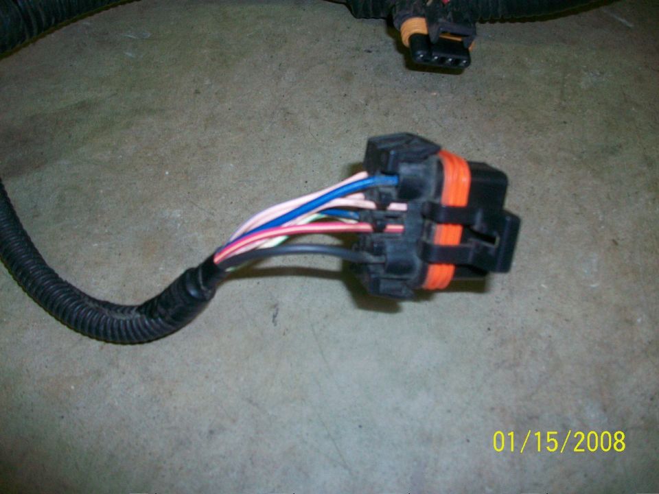 Wiring harness connector with orange and black housing and multiple colored wires, on a concrete surface