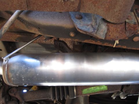 1996 Ford Bronco - Undercarriage view of a vehicle's exhaust system, showing a shiny muffler and rusty frame components.