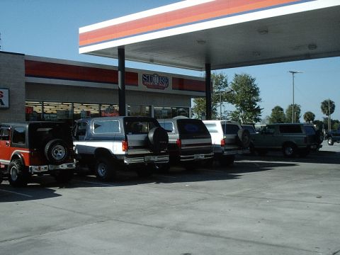 1996 Ford Bronco - Several SUVs, including a 1996 Ford Bronco, are parked at a gas station on a sunny day.