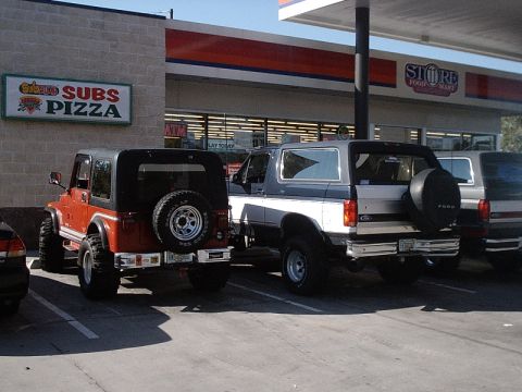 1996 Ford Bronco - Two SUVs are parked in front of a store with a pizza and subs sign.