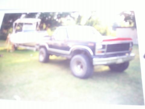 1993 Ford Bronco - A dark blue Ford Bronco is parked on a grassy area, with a boat on a trailer visible behind it.