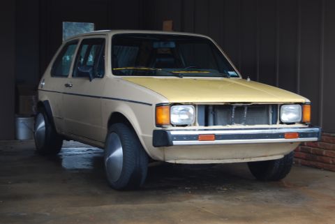 1983 Volkswagen Rabbit - A tan 1983 Volkswagen Rabbit with a yellow hood is parked indoors, showing its front end with a missing grille.
