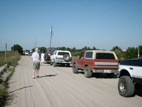 1996 Ford Bronco - Several off-road vehicles are lined up on a dusty track under a clear blue sky.