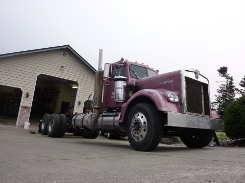 1959 Kenworth W900A - This purple Kenworth semi-truck cab is parked outside a garage, showing its distinctive front end and side profile.