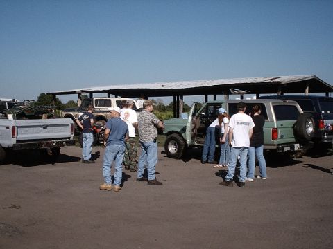 1996 Ford Bronco - Several people stand around a green SUV parked under a shelter with other vehicles nearby.