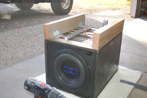 1992 Ford F-150 - A subwoofer box with a wooden frame is shown, with a drill in the foreground and part of a vehicle in the background.