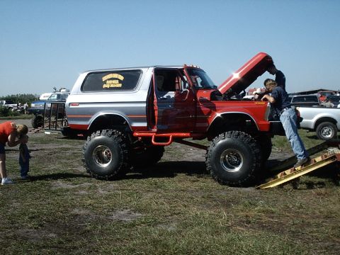 1996 Ford Bronco - A lifted red and silver SUV, likely a 1978 Ford Bronco, is parked with its hood open while people attend to it.