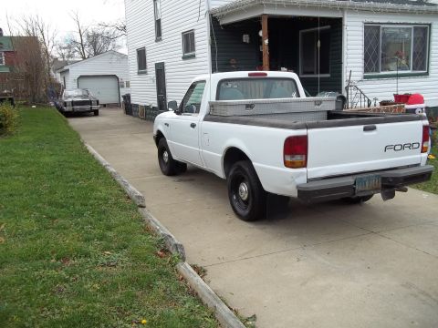 1970 Ford Ranchero - A white Ford pickup truck is parked in a driveway next to a house, with another vehicle visible in the background.