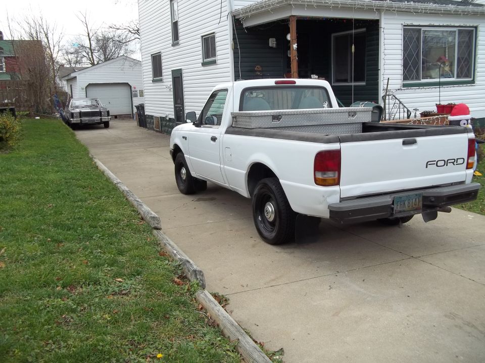 White Ford pickup truck parked in driveway, another car in background