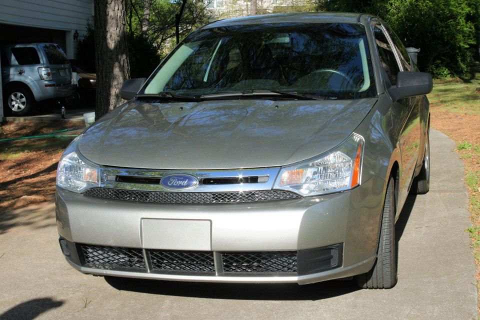 Silver Ford sedan parked on a driveway, front view. Another silver SUV is visible in the garage