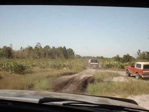 1996 Ford Bronco - Two vehicles, a red Bronco and a pickup, navigate a muddy track in a rural landscape.