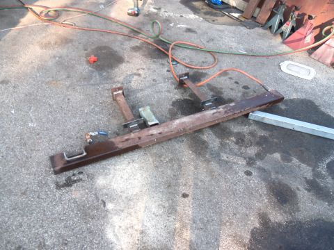 1989 Ford Bronco - A rusty metal frame with attached brackets and hoses lies on a concrete surface, possibly in a workshop or driveway.