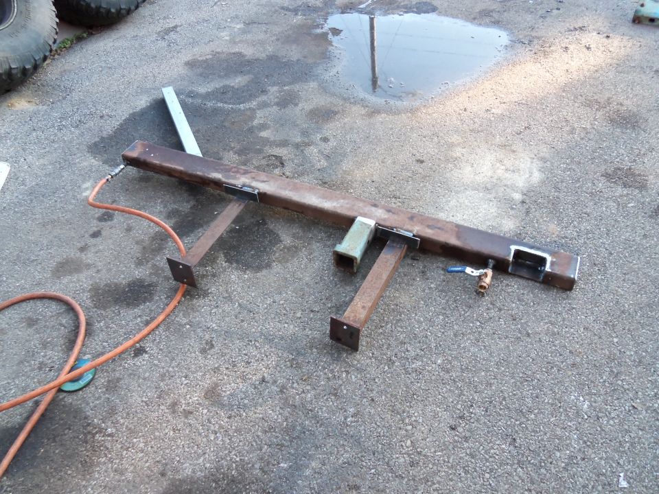 Rusty metal frame with two legs, an air hose, and a valve attached, resting on asphalt