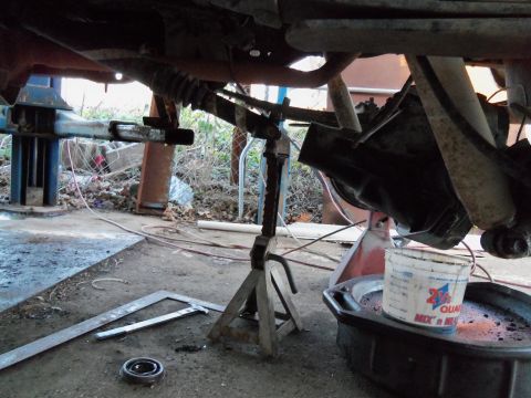 1989 Ford Bronco - Undercarriage view of a rear axle assembly, including the differential and shock absorber, with a drain pan and tools nearby.