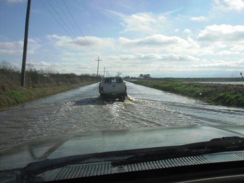 1993 Ford Bronco - A white pickup truck navigates a flooded road, with another vehicle following behind.