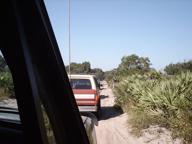 Two-tone tan and maroon vehicle ahead on a sandy trail seen through a car window