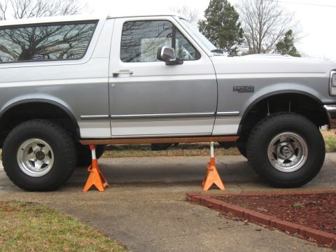 1994 Ford Bronco - A 1994 Ford Bronco is shown on jack stands, highlighting its side profile with a two-tone silver and white paint scheme.