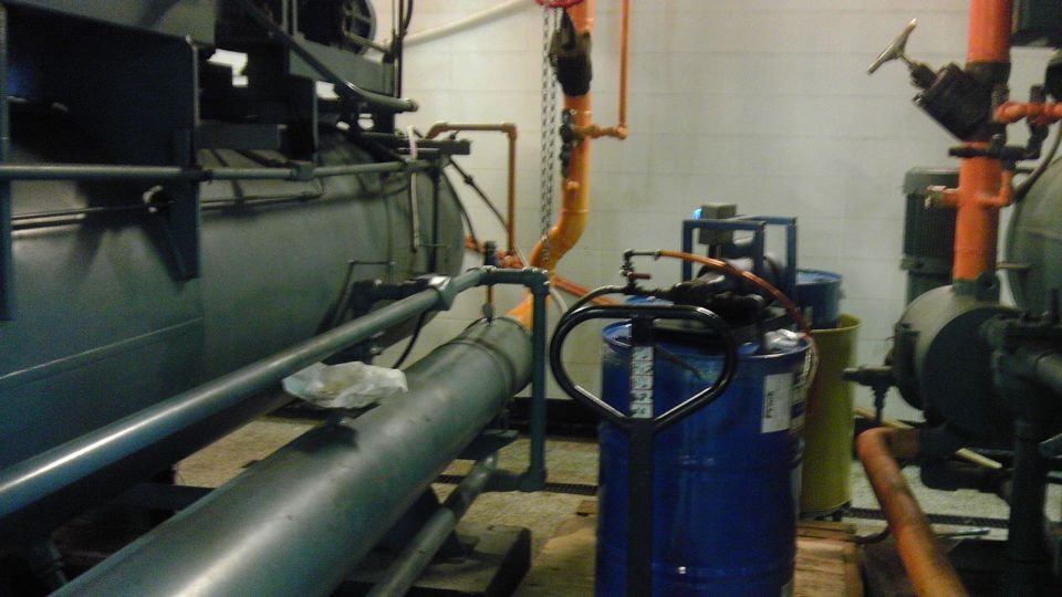 Industrial pipes and machinery in a room with blue barrels and a pallet jack