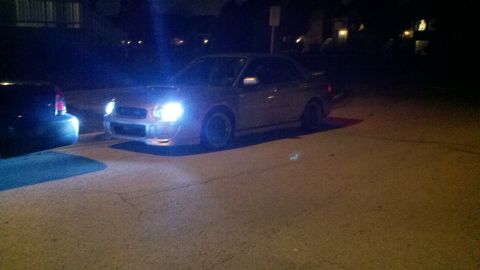 1999 Mercury Grand Marquis - A silver Subaru Impreza WRX is parked on a street at night, with its headlights illuminated.