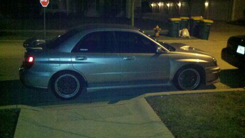 1999 Mercury Grand Marquis - A silver Subaru Impreza WRX is parked on the side of the road at night, with trash cans and a stop sign visible in the background.
