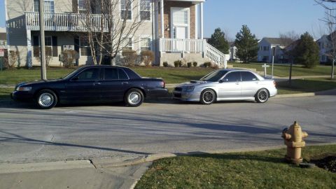 1999 Mercury Grand Marquis - Two sedans are parked on a residential street in front of an apartment building.