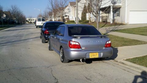1999 Mercury Grand Marquis - A silver Subaru Impreza WRX sedan is parked on the street behind a black car and a white van.