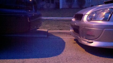 1999 Mercury Grand Marquis - Two cars are parked close together on a street at dusk, with one car's front end visible.