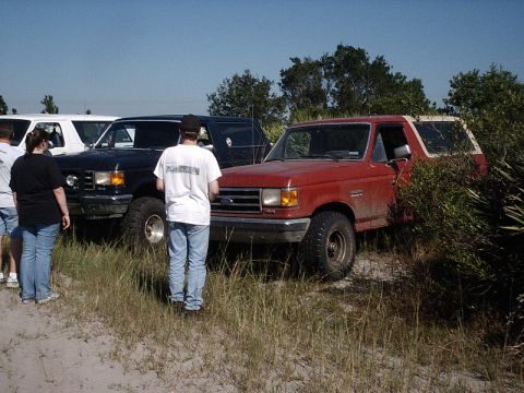 1996 Ford Bronco - Two Ford Broncos are parked in a grassy area with people standing around them.