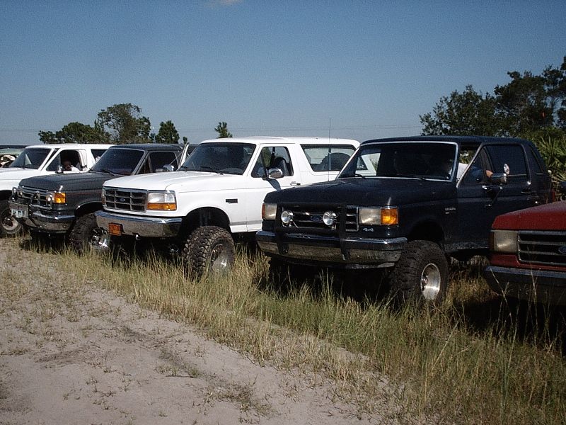 Row of lifted Ford Broncos and trucks parked in a sandy field
