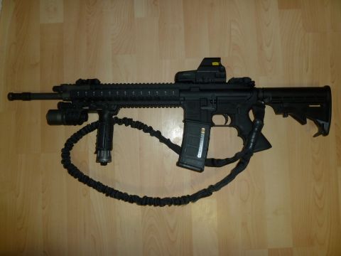 1992 Ford Mustang - An AR-15 style rifle is displayed on a wooden floor, equipped with a red dot sight, vertical foregrip, and a tactical sling.