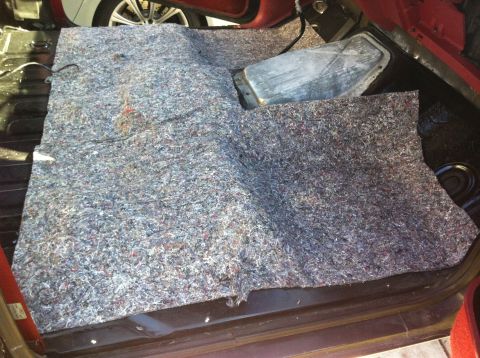 1991 Ford Bronco - The interior floor insulation of a red vehicle is visible, with a metal component protruding from the carpeted area.